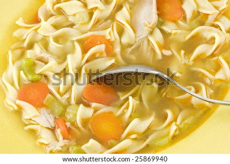 Homemade chicken noodle soup with carrots and celery in a yellow bowl, macro with copy space