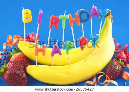 Candles spelling Happy Birthday stuck in bananas instead of cake for healthy lifestyle birthday, blue background with copy space