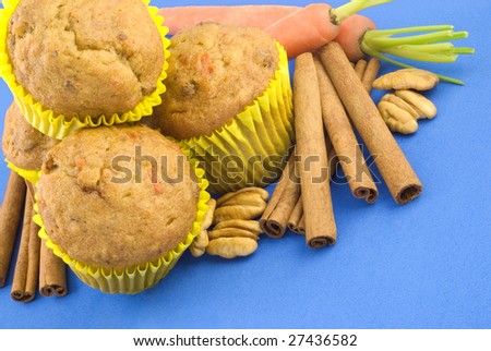 A stack of carrot nut muffins on a blue background with carrots, cinnamon sticks and pecans, copy space