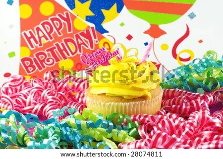 A colorful Happy Birthday Cupcake with one unlit candle with birthday decorations and Happy Birthday message