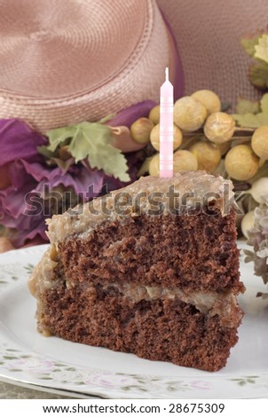 A delicious moist slice of homemade German Chocolate Cake on a plate with one unlit pink candle and vintage decorations, vertical with copy space