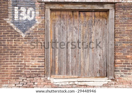 An aged boarded window on a cracking red brick wall with an arrow and a number on the wall, copy space
