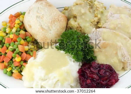 A Thanksgiving meal, with sliced turkey, dressing, mashed potatoes with gravy, mixed vegetables, cranberry relish and a roll, closeup