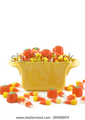 Halloween candy in a yellow dish, candy corn, candy pumpkins, spilling out on white vertical background, copy space