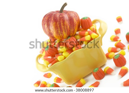 A yellow bowl full of Halloween candy, candy corn, and candy pumpkins, diagonal viewpoint, with pumpkin on top of candy, horizontal with copy space