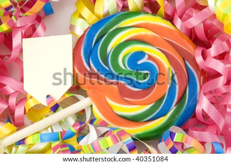 A colorful swirling birthday sucker with blank tag, ribbon background with selective focus, and copy space