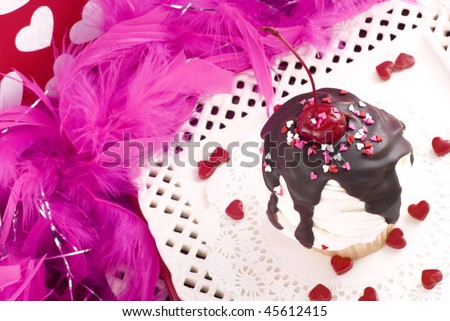 Valentine sundae cupcake with white frosting, fudge, and a cherry on top, with pink boa, closeup, horizontal