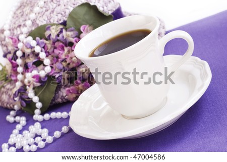 A cup of hot morning coffee with vintage hat and pearls on a purple placemat, diagonal viewpoint with copy space