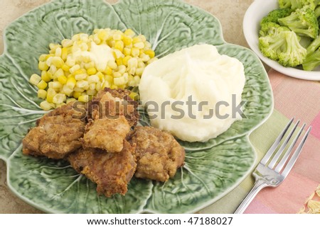 A meal of fried pork tenderloin, mashed potatoes and buttered whole kernel corn with a side of steamed broccoli, horizontal with selective focus