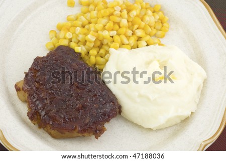Barbecue pork loin chop with buttered mashed potatoes and whole kernel corn on a plate, horizontal closeup, selective focus