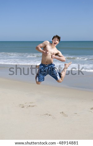 Male teenager jumping on a beach, happy expression with thumbs up, ocean and sky background, vertical with copy space