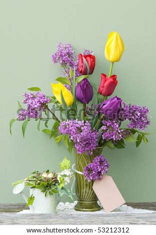 A vase of bright colored tulips and lilac in a vase with a blank gift tag and spring decorations, vertical