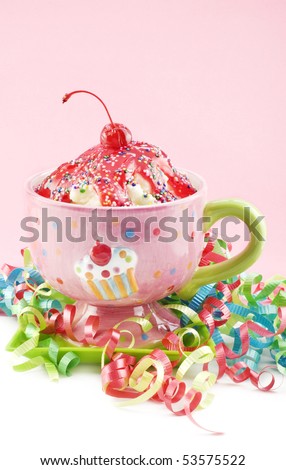 An ice cream sundae topped with cherry sauce, curly party ribbons, with pink background