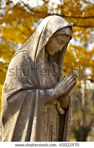 A cemetery statue of Mother Mary with autumn leaves in background, selective focus