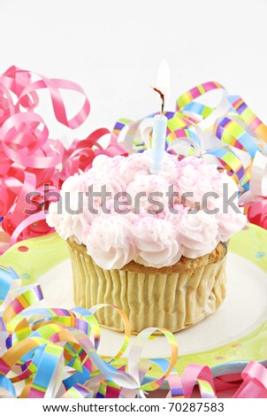 A homemade birthday cupcake with one lit candle, white background with curly ribbons