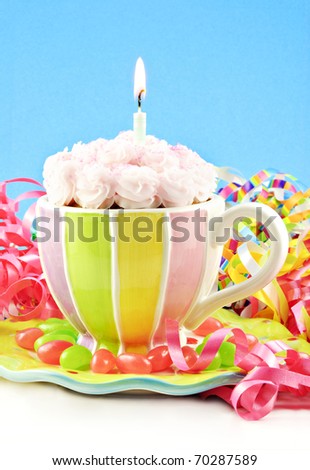 A colorful homemade birthday cupcake in a cup with one lit candle, blue vertical background with copy space