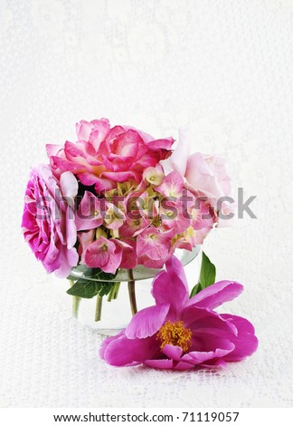 A glass vase of fresh cut flowers on a white lace background with copy space