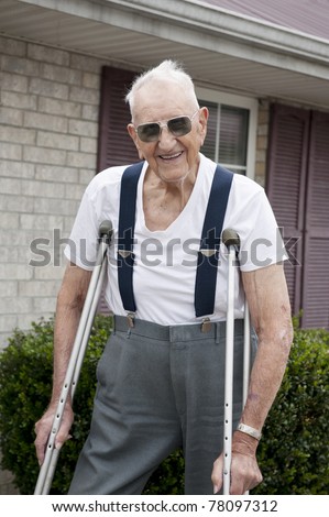 A 93 year old elderly man with crutches, standing alone outside his apartment with a big smile on his face