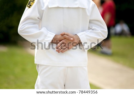 A US Navy solider in white uniform standing with hands folded behind him, back view with shallow depth of field