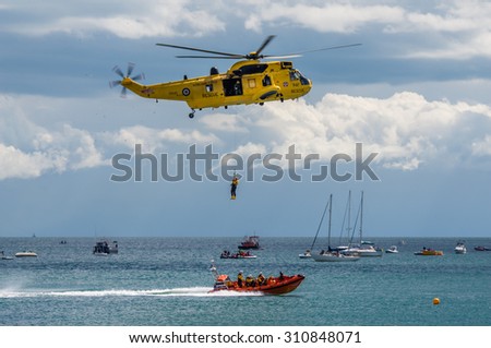DAWLISH, UNITED KINGDOM - AUGUST 23, 2014: Royal Navy Sea King Search and Rescue Helicopter Flying at the Dawlish Airshow Demonstrating Winch Rescue with an Inshore Lifeboat