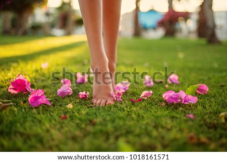Close up female crossed legs walking on the grass,pink flowers on the grass.