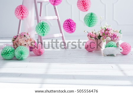 The original bright decor for birthday girl.Pink and green decorative paper balls. White Room decorated with flowers and paper decorations for party.Small white rabbit
