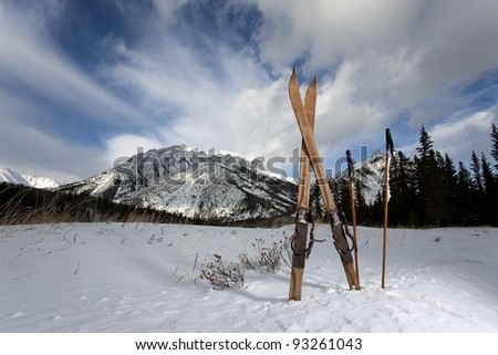 vintage skis in snow with mountains and clouds in the background