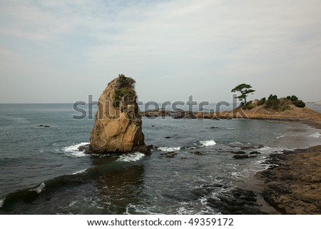 Rock with pine trees and a single finger-like rock at a seashore in a day after rain