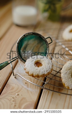 Homemade Linz biscuits on a grate with powdered sugar and a glass of milk, vertical orientation