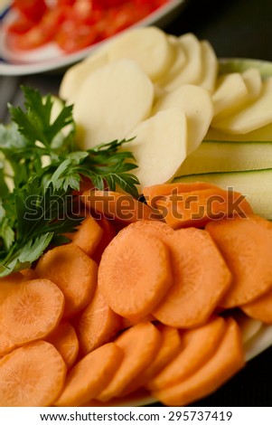 Tomatoes, potatoes, carrots and parsley cut on a plate on a black background