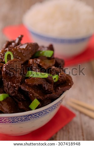 Concept of Chinese food. Beef cooked in soy sauce with spring onions and star anise served in a china bowl. Chopsticks and bowl of rice in the background. Selective focus.