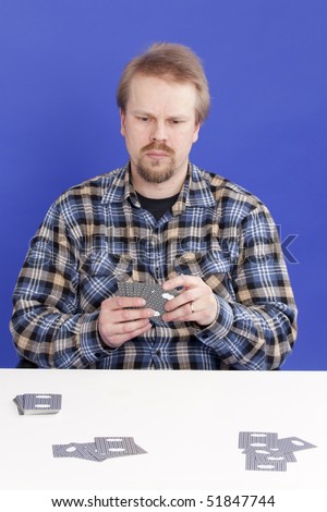 Man Plays Solitaire Card Game at a white table. Studio photograph.
