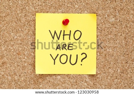 Who Are You written on an yellow sticky note pinned on a cork bulletin board.