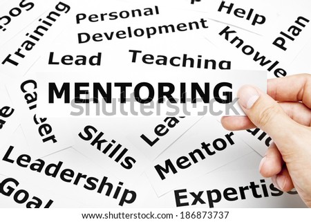 Hand holding a piece of paper with the word Mentoring on it.