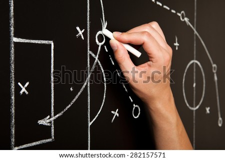 Hand drawing a soccer game tactics with white chalk on blackboard.