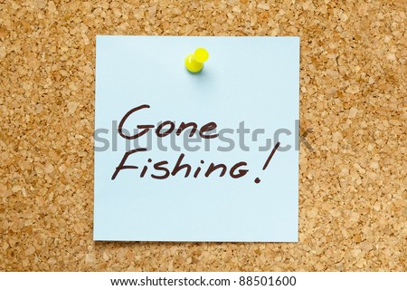Gone Fishing! written on blue sticky note pinned on office cork bulletin board.
