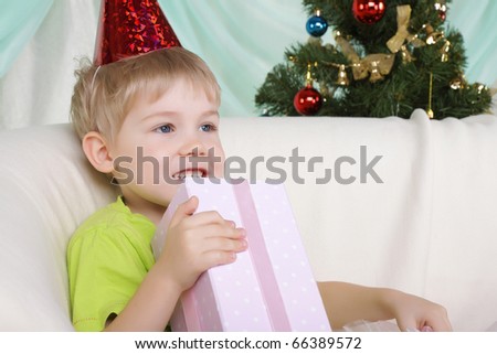 Little boy near to christmas fur-tree sits with gift