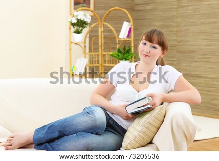 Young attractive woman with book lays on a sofa