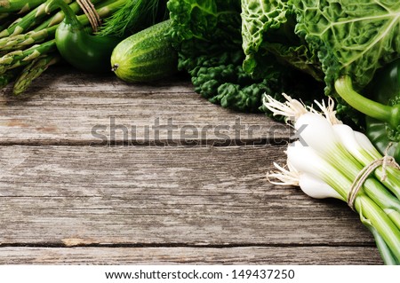 Frame with green organic vegetables on wooden background