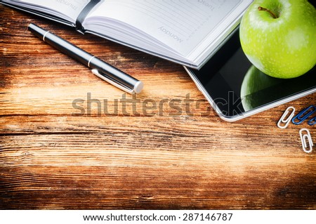 Desktop with paper agenda, digital tablet and green apple