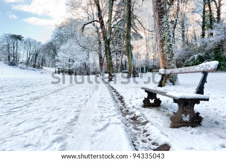 Bench in a snow covered park at sunset