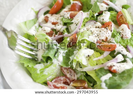 A house salad containing leafy greens, grape tomatoes, red onions, ranch dressing, and fresh cracked black pepper