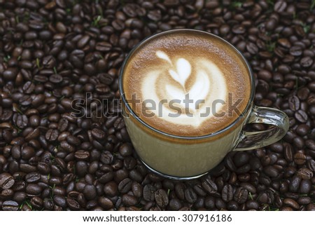 A cup of coffee with flower shape milk foam on coffee bean background