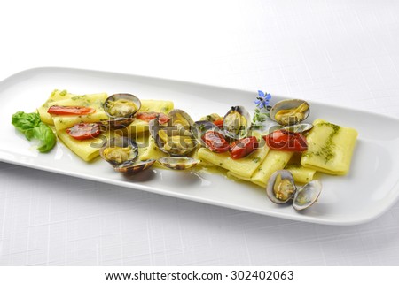 Pasta Dish Paccheri Macaroni with Clams Grilled Tomatoes and Basil Sauce in long white plate