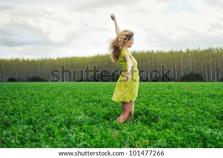 Portrait of a beautiful blonde girl, dressed with a green dress, with open arms in a meadow