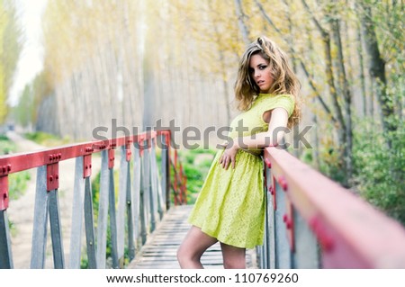 Beautiful blonde girl, dressed with a beige dress, standing in a rural bridge
