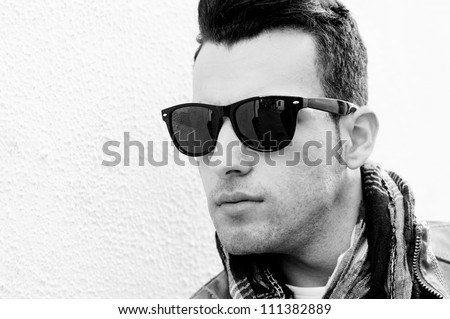 Portrait of a young handsome man, model of fashion, wearing tinted sunglasses in urban background