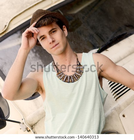 Portrait of a young handsome man with an old van wearing a sun hat