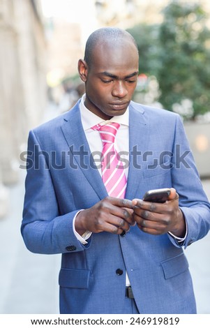Portrait of a black businessman wearing suit reading his smart phone in urban background