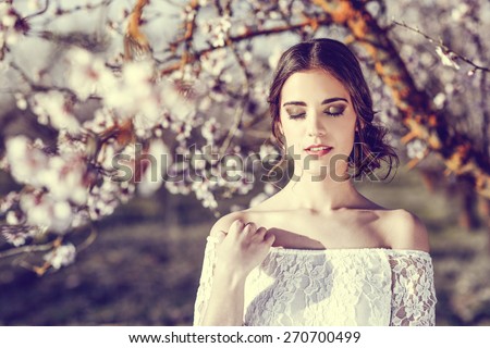 Portrait of young woman in the flowered garden in the spring time. Almond flowers blossoms. Girl dressed in white like a bride.